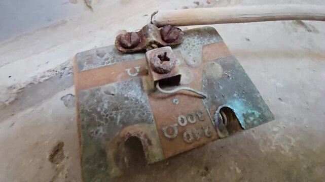 Macro shot of a corroded water heater electrical connector with heavy rust and green oxidation. Close-up view highlights damaged terminals and resistance markings on a weathered metal surface.
