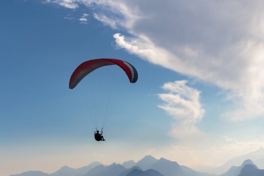 Paraglider Soaring Over Mountain Range Against Blue Sky