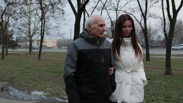 Elderly father and his adult daughter enjoying a walk in the park while having a conversation. Demonstrating family love. Care. And intergenerational connection during their leisure time outdoors