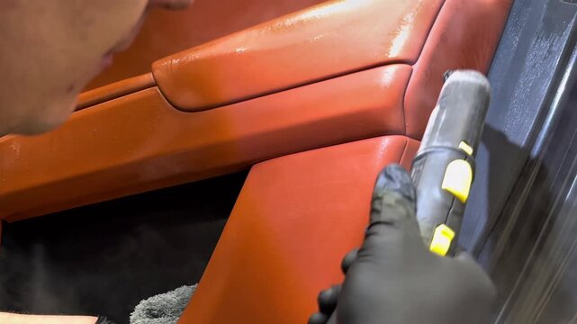 Car detailing and the concept of car interior care. The detailing master cleans the car interior with a hot steam cleaner close-up. Dry cleaning of the car interior, close-up, selective focus. 