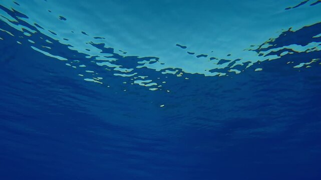 Underwater view of fine ripples on the surface of crystal clean blue water in front of a turquoise sky in calm weather. Natural undersea background of water surface in calm 