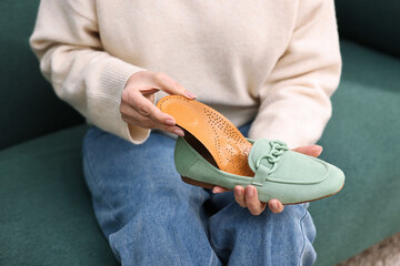 Senior woman putting orthopedic insole into shoe indoors, closeup