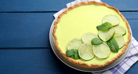 Tasty lime pie with fruit slices and mint leaves on blue wooden table, closeup. Space for text © New Africa