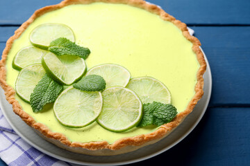 Tasty lime pie with fruit slices and mint leaves on blue wooden table, closeup © New Africa