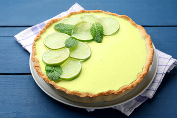 Tasty lime pie with fruit slices and mint leaves on blue wooden table, closeup © New Africa