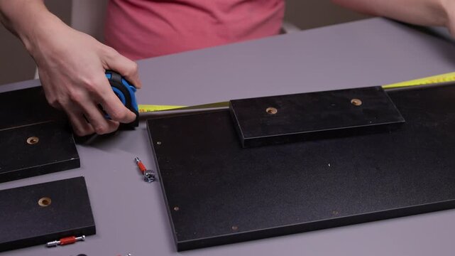 Craftsman measuring dimensions of flat packed furniture parts using yellow tape measure, focusing on preparation steps for assembly and construction in dark carpenter shop, close-up, slow motion.