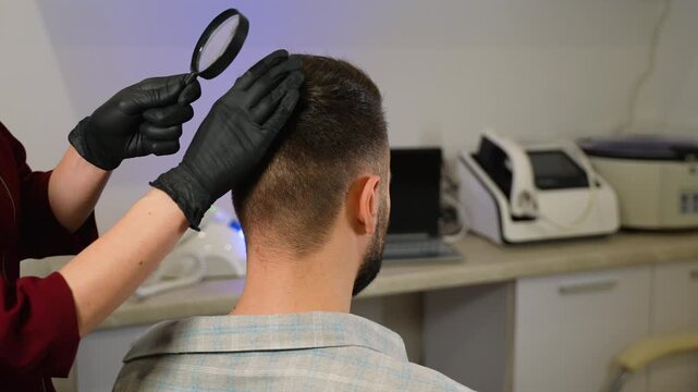 Trichologist examining man's hair and scalp with magnifying glass