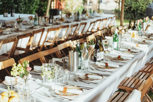 Table setting, wooden folding chairs along long tables cheerfully set with decorations like flowers for dinner outdoor at daytime in summer at a wedding.