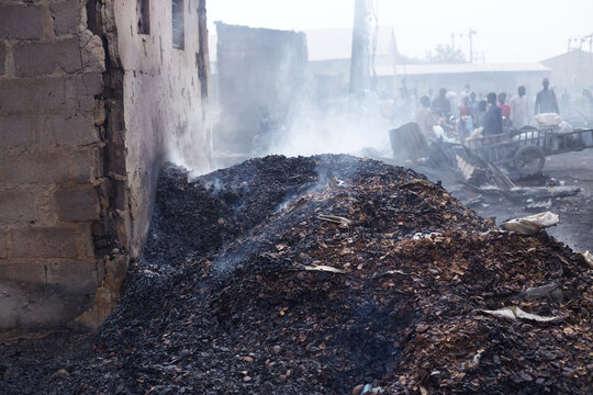 Kano, Nigeria - 27 January 2024: View of charred debris smoldering beside a damaged building near Dakata fire service, with onlookers in the background.