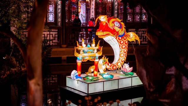 Portland, United States - 17 February 2026: View of a vibrant, illuminated carp lantern, perched atop a platform amidst the tranquil Lan Su Chinese Garden's traditional architecture.