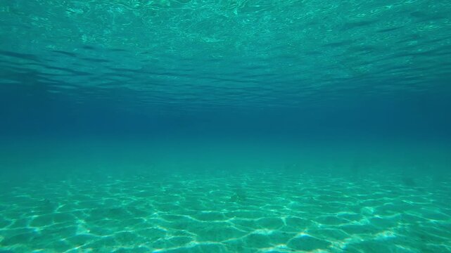 Moving forward in turquoise water over a sandy seabed with the sun glinting on the sand reflected in the emerald water surface during the calm sea, Natural underwater background
