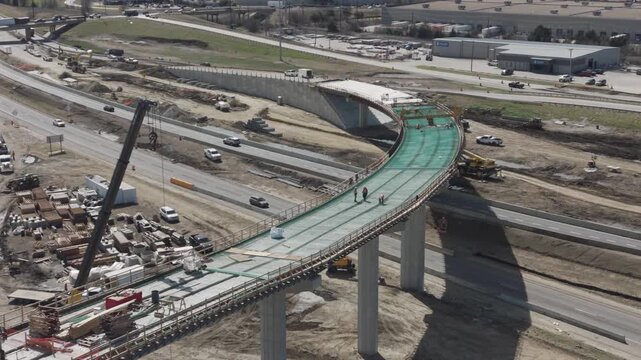 Denton, Texas USA &ndash; February 18, 2026: Construction workers on an elevated bridge ramp under construction at a highway interchange with vehicles traveling on surrounding roadways.