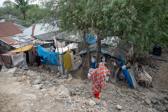 Satkhira, Bangladesh - 25 April 2025: View of a woman in a vibrant orange and white patterned garment walking towards makeshift homes with corrugated iron roofs.