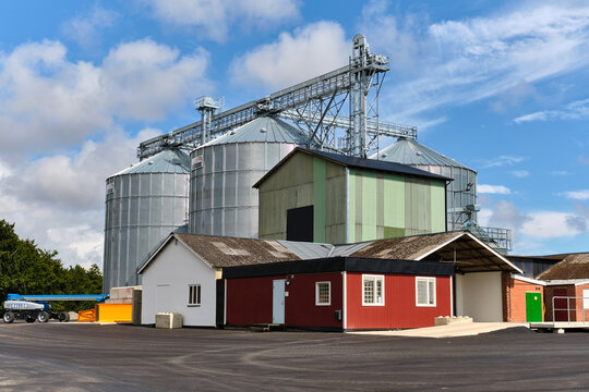 Lund, Sweden - 23 July 2025: View of the silvery grain silos gleaming under the bright sky, contrasting with the red and white buildings below, a blend of industrial strength and rural charm.