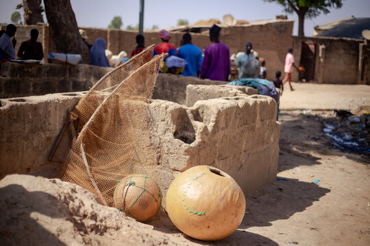 Argungu, Nigeria - 12 February 2026: View of fishing nets and gourds resting on sun-baked earth, near weathered mud structures where locals gather, creating a scene of rustic, everyday life.