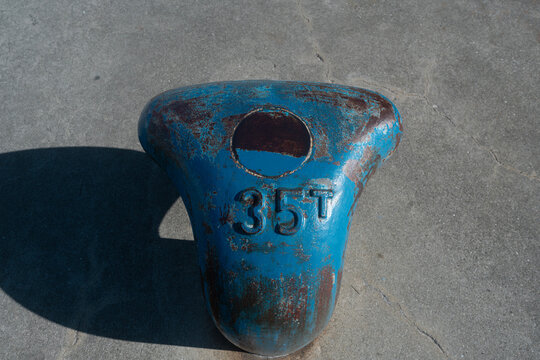 Primer plano de una bita de amarre marina de metal azul desgastada con la marca "35T" sobre hormig&oacute;n.