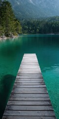 Fototapeta premium Wooden dock leading over emerald lake toward forested mountains with clear turquoise water and rocky shoreline under soft daylight