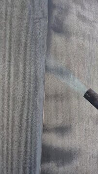 Vertical 9:16 slow motion diagonal shot of a gas torch melting bituminous membrane for foundation waterproofing.