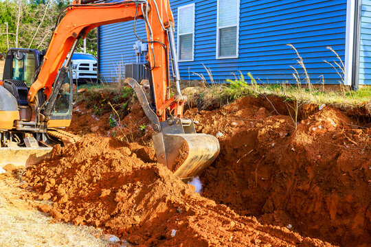 Excavator digs trench near building in residential construction area