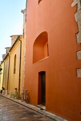 Fototapeta premium Ruelle colorée de Saint-Tropez avec vélos appuyés contre des façades jaunes et orange, sous la lumière du soleil, illustrant le charme méditerranéen et l’authenticité du village.
