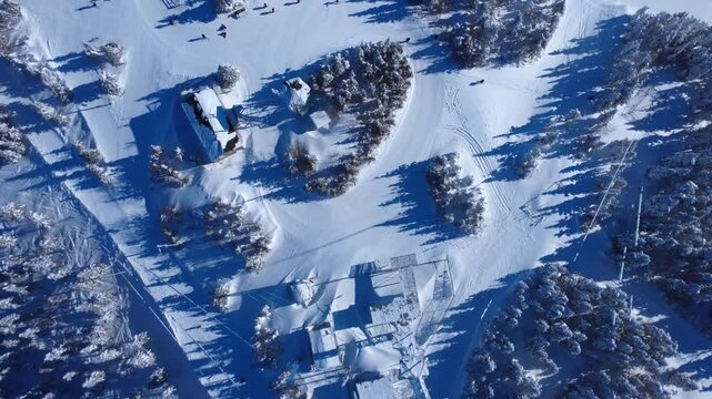 Top-down drone footage of skiers exiting lifts and gliding down groomed slopes through snowy pines and chalets at Val d'Irene, Quebec. High-angle winter sports scenery under bright sunlight.