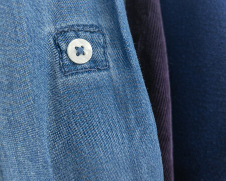 White button on a stitched tab detail of a light blue denim or chambray shirt 