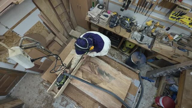 Mesmerizing Slow Motion Swivel Pan of Master Craftsman in Extreme Protective Hood Surfacing Raw Timber Slab inside Cluttered Maker Studio for Bespoke Furniture Production