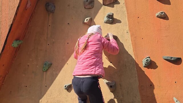 Young girl finishing bouldering route and jumping down from outdoor climbing wall