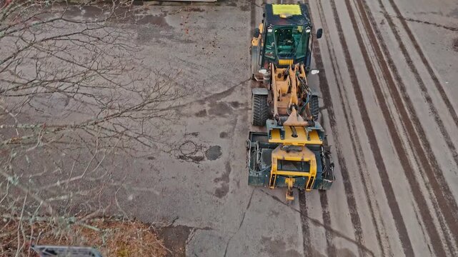 Industrial street sweeper attachment on a wheel loader working on a Finnish parking area.