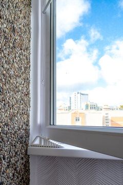 Silicone retainer for window frame when opening window. Modern interior corner with textured pebble wall and plastic window overlooking city buildings