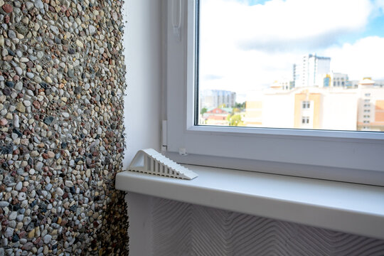 Silicone retainer for window frame when opening window. Modern interior corner with textured pebble wall and plastic window overlooking city buildings