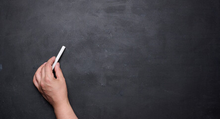 Naklejka premium A close-up of a woman's hand holding a piece of white chalk, ready to write on a blank