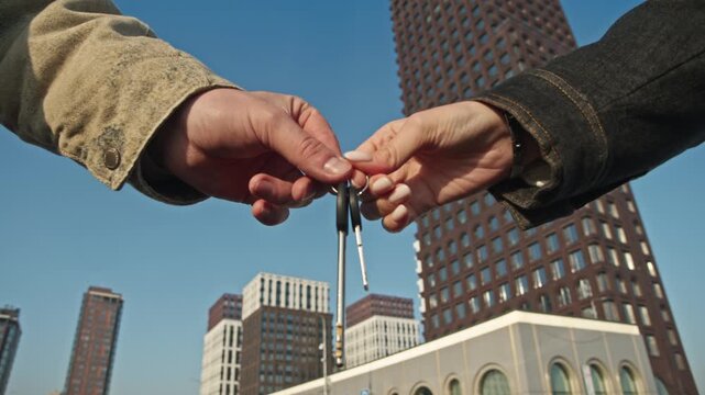 Apartment purchase scene: realtor in female hand passes keys to client near brick high-rise.