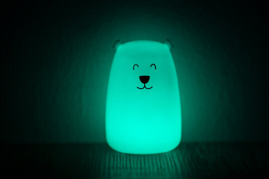 Cute glowing bear shaped night light lamp emitting soft teal light in a dark cozy room