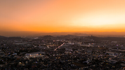 Obraz premium Aerial cityscape at sunset with glowing orange sky and illuminated urban lights