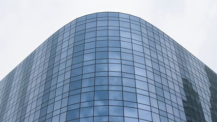 Obraz premium A sleek, modern skyscraper with a curved glass facade against a cloudy sky
