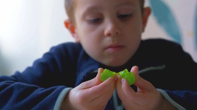 Young Boy Closely Examining Green Jelly Candy in Hands with Focused Concentration &mdash; Childhood Curiosity, Sensory Exploration and Mindful Attention Concept