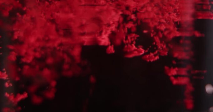 Soft focus close up of pink acrylic paint particles diffusing in dark liquid, forming a gentle abstract texture suitable for creative, beauty, or cosmetic themed designs. Slow motion.