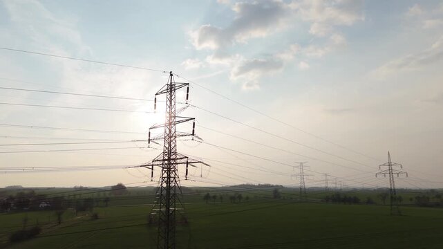 Aerial drone rising shot of high voltage electricity pylons row across green fields at sunset