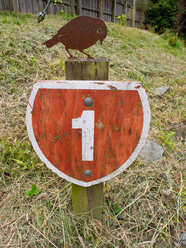 Rustic weathered New Zealand State Highway 1 road sign with metal bird