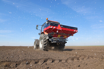 Spreading mineral fertilizer, low angle shot. Farmer with agricultural machinery fertilizing agricultural field in spring time. © branex