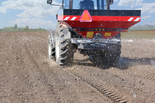 Spreading mineral fertilizer. Farmer with agricultural machinery fertilizing agricultural field in spring time.