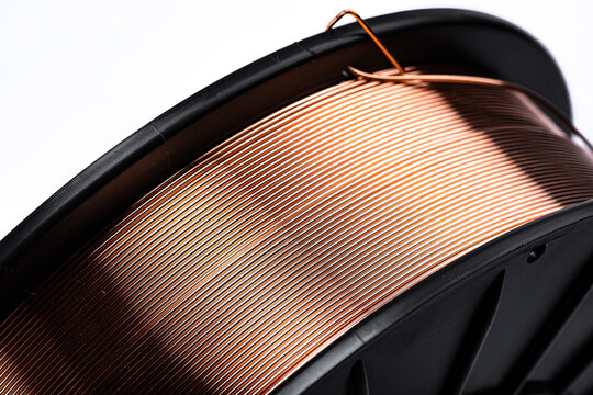 Precision wound copper welding wire on black plastic spool. Detailed shot of copper coated welding wire on a black reel showing winding pattern.