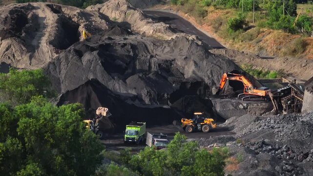 Heavy machinery including excavators, loaders, and dump trucks actively working in an open-pit mine, extracting and processing volcanic sand for industrial use and construction on Bali, Indonesia
