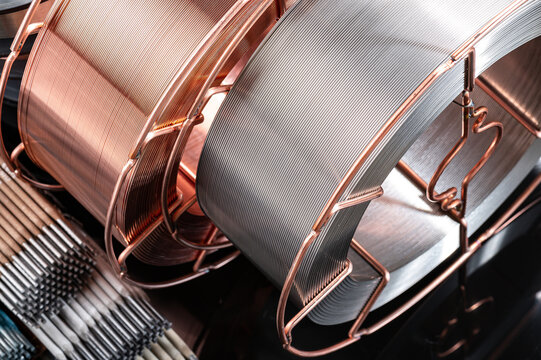 Close up of copper and steel welding wire reels. Detailed view of two different types of welding wire coils on a dark reflective surface.