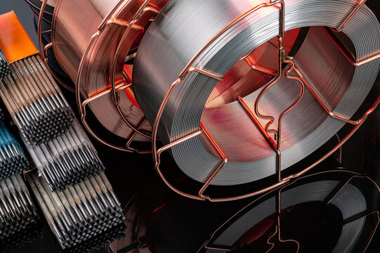 Close up of welding wire spools with red illumination. Metal and copper welding wire reels on black background with red backlighting and reflections.