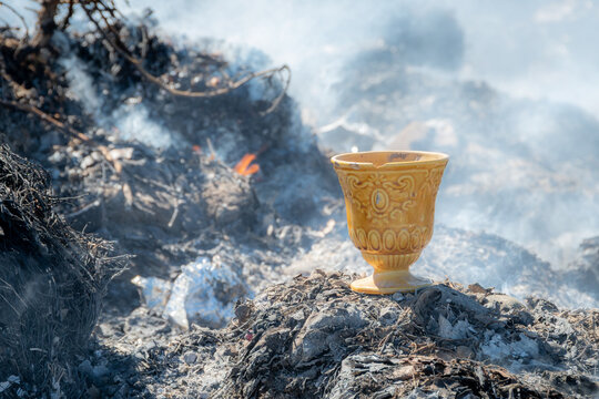 copa biblica de la serie de surrealismo , donde se encuentra en un basurero rodeada de basura quemandose , que genera ese humo en su atmosfera , copa de ceramica con dibujos y  color amarillo dorado