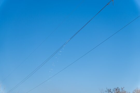 Ice falling from a diagonal power wire against a clear blue winter sky.