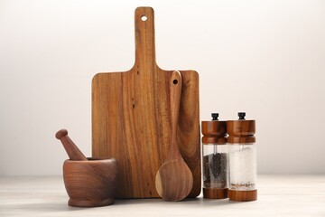 Cutting board, kitchen utensils and spices on table near white wall