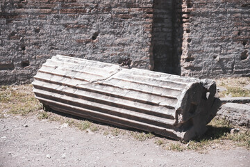 Naklejka premium An ancient column lies on the ground among the remains of a structure. The column shows signs of wear with detailed grooves and is part of a historic site.